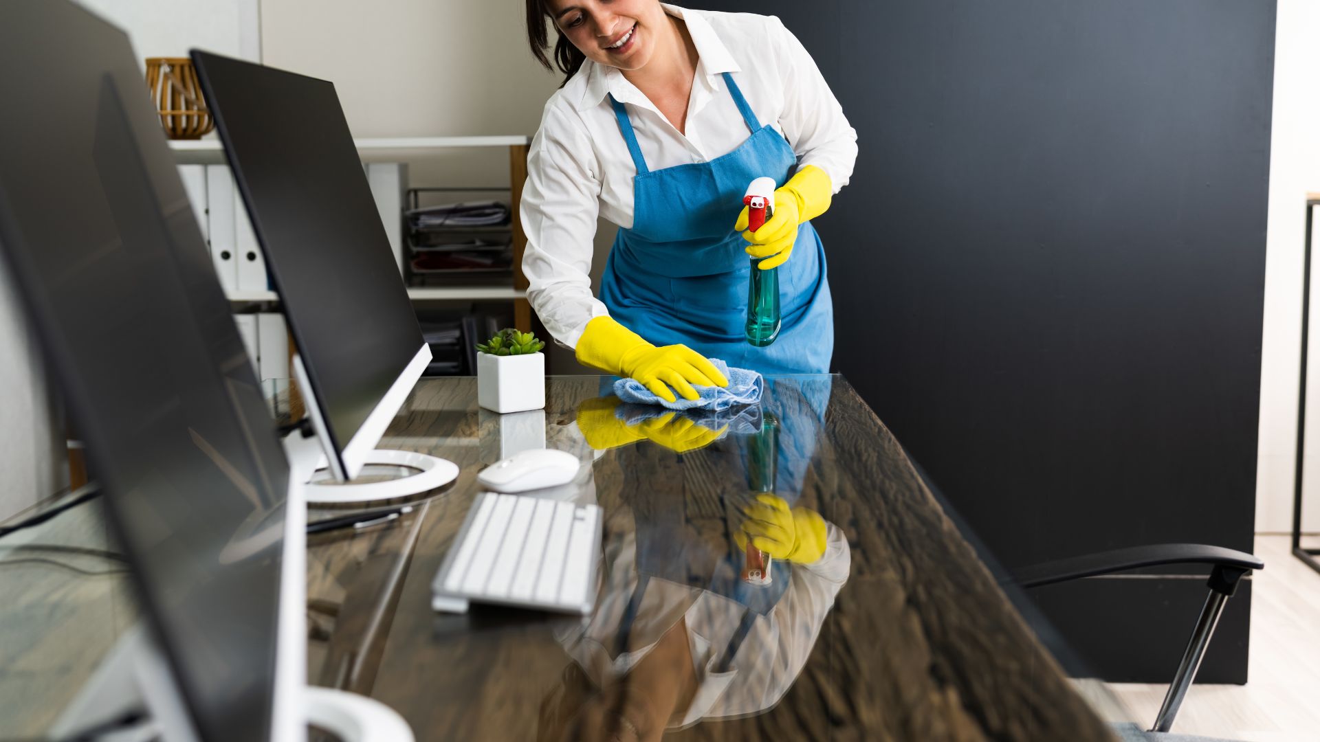 A woman cleaning a desk with a yellow glove